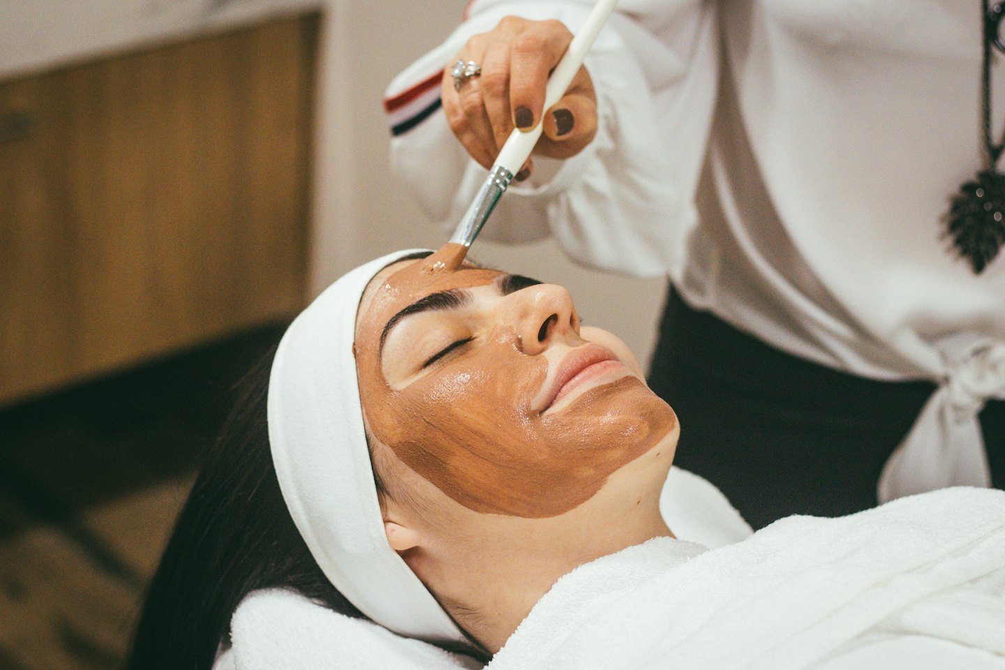 Esthetician applying face mask to client during spa treatment.
