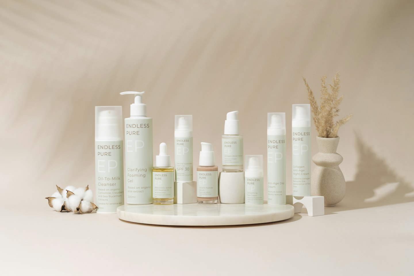 Skincare products arranged on a marble tray with cotton and pampas grass.